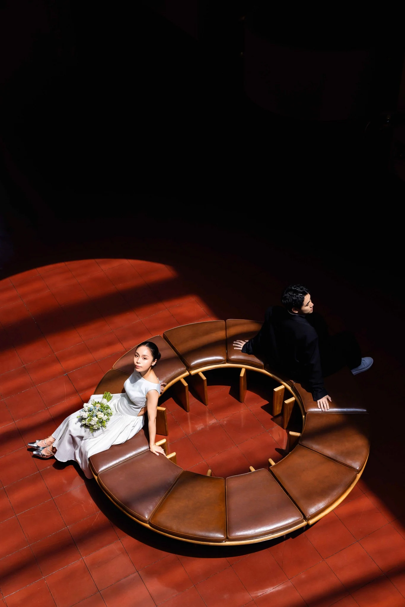 Bride and groom at opposite ends of a curved bench on a red floor